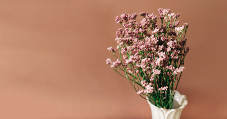 Small pink flowers known as sea lavenders with green stems in a vase against a rose taupe color background. Spring themed social media banner with copy space.