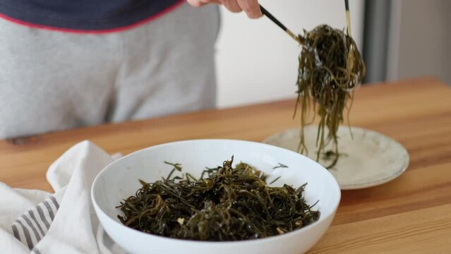 Bowl with seaweed salad on a wooden table. Man prepares seaweed salad at home.