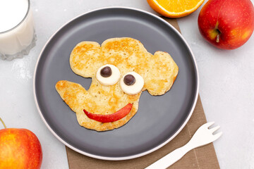 Funny elephant face shape snack from pancake on plate. Cute kids childrens baby's sweet dessert, healthy breakfast,lunch, food art with milk,apples,orange on gray concrete background,top view