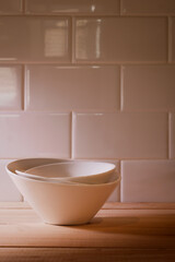 Three stacked white porcelain bowls with warm light on wood planks.