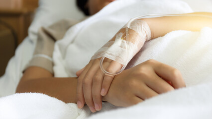Photo of a hand with an IV in a hospital.Asian woman lying sick in hospital