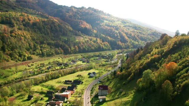Colorful leaves covering steep hillside with a village in the background. Drone footage of cinematic backcountry with winding highway and charming cottages. High quality 4k footage