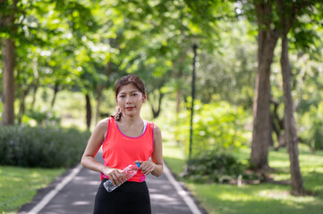 Asian female runner standing outdoors holding water bottle in the park