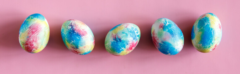 Colorful handmade Easter eggs painted like Earth on pink paper background. Minimal happy Easter holiday conceprt. Top view flat lay, banner or header.
