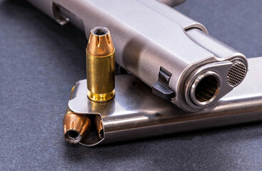 A stainless steel 1911, 45 ACP pistol with a loaded magazine and an additional bullet on a black...