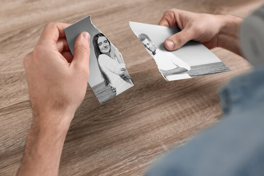 Divorce and breakup. Man holding parts of ripped black and white photo at table, closeup
