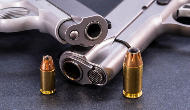 Two stainless steel 1911 pistols, one a 45 ACP and the other a 380 caliber with a hollow point bullet for each next to it on a black background
