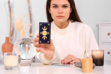 Soothsayer predicting future at table indoors. Focus on tarot card