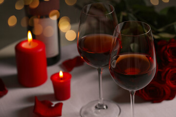 Romantic table setting with glasses of red wine, rose flowers and burning candles