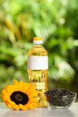 Sunflower cooking oil, seeds and yellow flower on light grey table outdoors