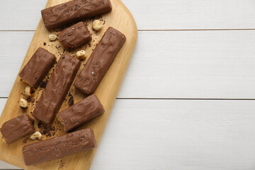 Board with delicious chocolate bars and nuts on white wooden table, top view. Space for text