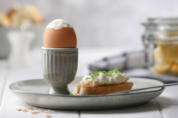 Fresh soft boiled egg in cup and sandwich on white wooden table