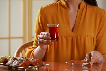 Woman holding glass of traditional Turkish tea at table indoors, closeup