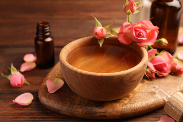 Bowl of essential oil and beautiful roses on wooden table. Aromatherapy treatment