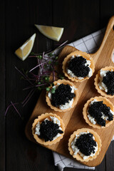 Board of delicious tartlets with black caviar and cream cheese on wooden table, top view