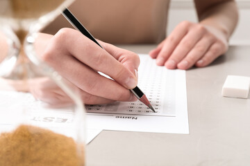 Student filling answer sheet at light grey table, closeup. Passing exam