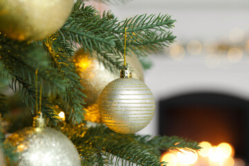 Beautiful golden Christmas balls hanging on fir tree branch against blurred background, closeup