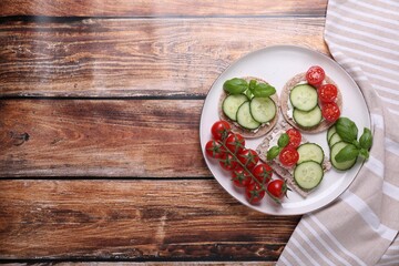 Plate with tasty crispbreads, cucumber, tomatoes and basil on wooden table, top view. Space for text