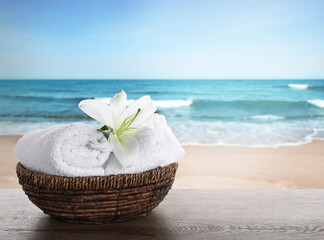 Fototapeta na wymiar Spa holiday. Fresh towels and lily flower on wooden table against seascape, space for text