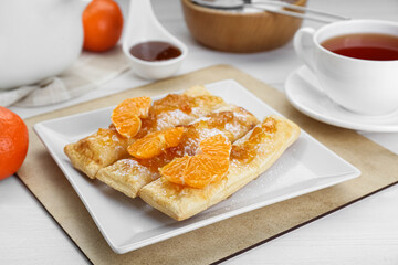 Fresh tasty puff pastry with sugar powder and tangerines on white wooden table, closeup