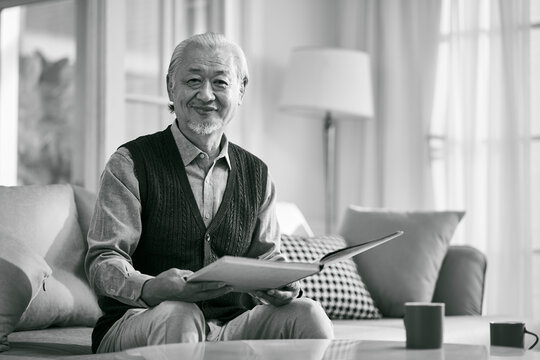 black and white portrait of a happy senior asian man reading a book at home