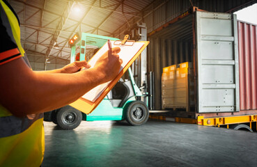 Worker Holds a Clipboard Checking the Loading Cargo Shipment at Distribution Warehouse. Forklift...