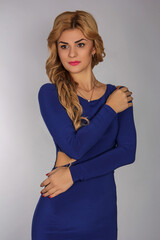 portrait of a blonde girl with blonde hair in a blue dress in a studio room, with makeup and hairstyle, red lips and manicure