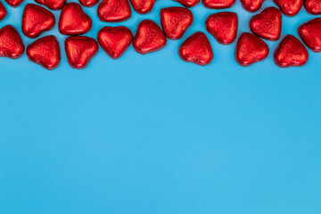 Heart shaped chocolates in red foil on blue background, flat lay, Valentine's day concept, copy space.