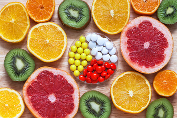 Bright background of fresh sliced healthy fruits and set of vitamins in form of tablets in center. Concept of taking care of health, boosting immunity, taking vitamin preparations. Flat lay, close-up