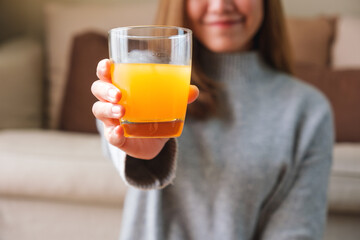 Closeup image of a woman holding and serving a glass of fresh orange juice