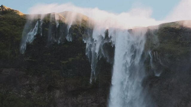 Static view of reverse waterfall in Iceland, mist blows up over top of cliff.