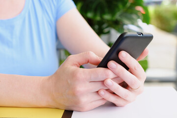 Close-up of a smartphone in female hands. Woman at the table of a street cafe surf the internet. Using smartphone, wasting time on social media, online shopping.