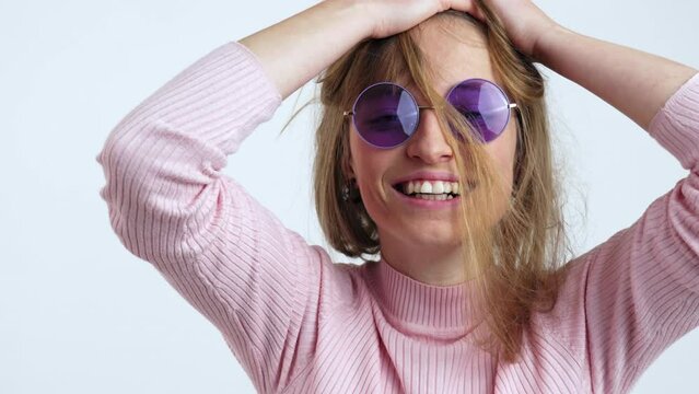 Happy young woman with purple glasses messing up her hair. Portrait slow motion shot isolated on white background