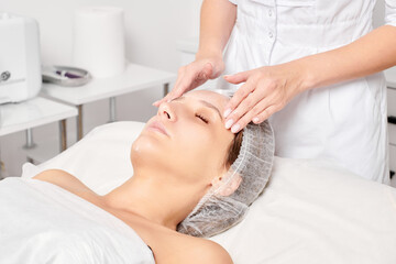 Cosmetologist rubbing moisturizing cream mask into woman face skin for rejuvenation, anti aging...