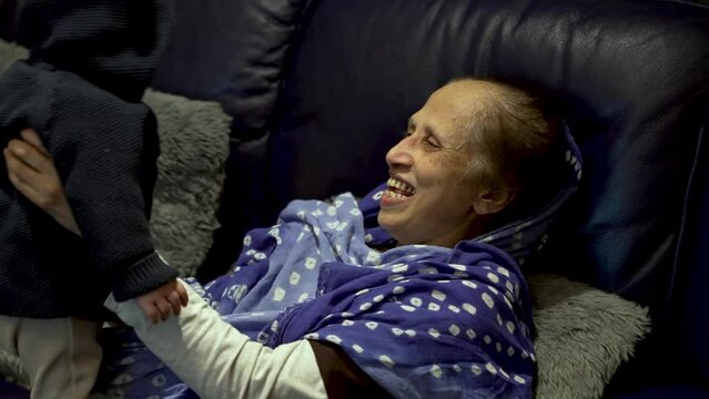 Bangladeshi Grandmother Playing With Her Grandson Indoors Sat On Sofa