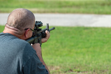 Bald middle aged man aiming for shooting a fully automatic rapid fire rifle
