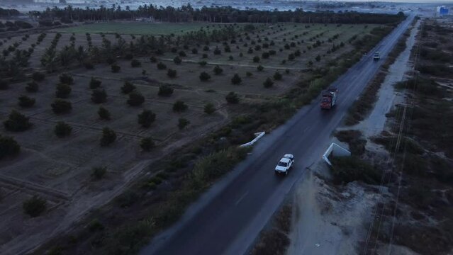 Aerial View Of Cars And Lorries Driving Along RCD Road Past Farmland In Baluchistan On Overcast Day