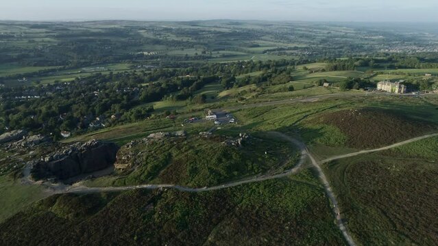 Establishing Drone Shot Flying Over Back of Cow and Calf Rocks in Ilkley down Rural Valley with Fields and Trees towards Burley in Wharfedale  at Golden Hour with Car Driving along Road West Yorkshire