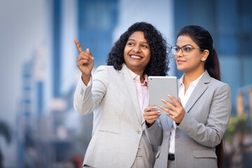 Two businesswomen working on a tablet outdoors.