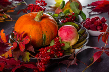 Pumpkin, apples and berries with autumn leaves on a textured table