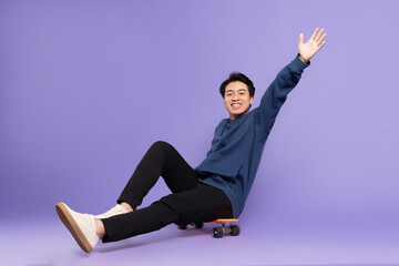 Image of young Asian man playing skateboard on purple background