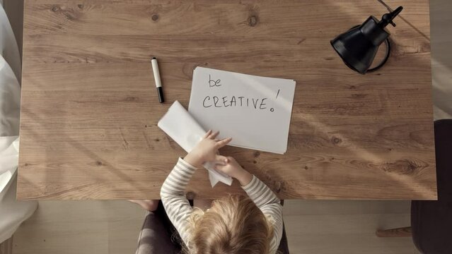Top down view of child, take paper with inscription THE END, crumples it and throws away. BE CREATIVE written on new paper. concept of end of failures and beginning of new life and trying.