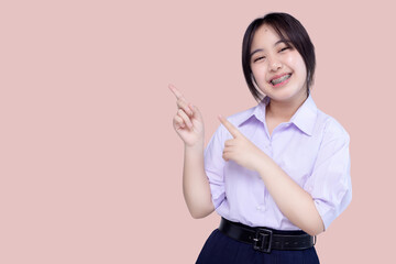 Happy pretty braces Asian school girl pointing finger to copy space isolated on pink background. - obrazy, fototapety, plakaty
