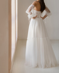 Fototapeta premium Back view of beautiful brunet bride dressed in the white long wedding dress with the naked back. Light chiffon wedding dress with with wide collapsible sleeves.