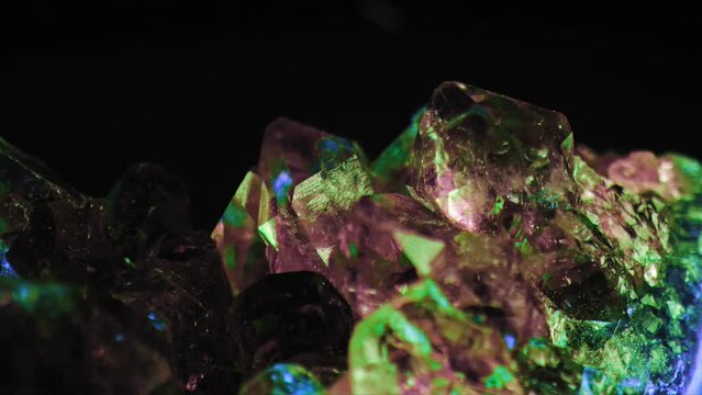 Luminous macro shot of purple amethyst crystal green and blue lighting against black background. Smooth panning for exquisite details.
