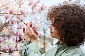 Teenager girl enjoy the smell and beauty of blooming magnolia flowers. Large flowering bush in the...
