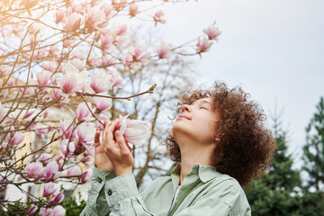 Teenager girl enjoy the fragrance and beauty of magnolia flowers. Large blooming bush in the spring...