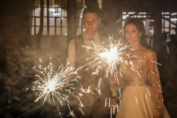 The bride and groom in a wedding dress in the sparks of fireworks at night.