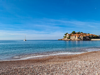 Luxury yacht floating next to idyllic island Sveti Stefan seen from sand beach, Budva Riviera, Adriatic Mediterranean Sea, Montenegro, Europe. Summer vacation in luxury hotel resort at seaside