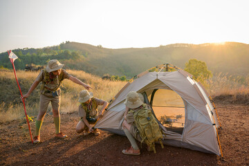 Boy Scout students attending a scout camp having good teamwork are setting up a tent to sleep in the camp in the evening as the sun sets. - obrazy, fototapety, plakaty